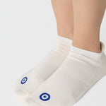Women wearing a solid white full foot grip sock with a blue evil eye motiff on the top of the toes, made for pilates, barre, yoga, and beyond.