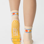 Women wearing an off white ivory ankle grip sock with a flower pattern wrapped around the ankle cuff and toes, made for pilates, barre, yoga, and beyond.