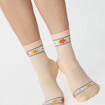 Women wearing an off white ivory ankle grip sock with a flower pattern wrapped around the ankle cuff and toes, made for pilates, barre, yoga, and beyond.