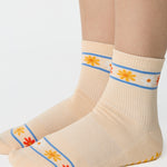 Women wearing an off white ivory ankle grip sock with a flower pattern wrapped around the ankle cuff and toes, made for pilates, barre, yoga, and beyond.