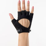 Woman wearing a pair of black grip gloves that has an opening for the fingers a breathable open back design, made for the studio and strength training. 