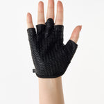 Woman wearing a pair of black grip gloves that has an opening for the fingers a breathable open back design, made for the studio and strength training. 