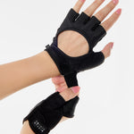 Woman wearing a pair of black grip gloves that has an opening for the fingers a breathable open back design, made for the studio and strength training. 