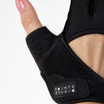 Woman wearing a pair of black grip gloves that has an opening for the fingers a breathable open back design, made for the studio and strength training. 