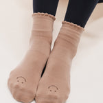 Women wearing brown ankle grip socks with black happy face for Pilates, Barre, Yoga, and beyond. 