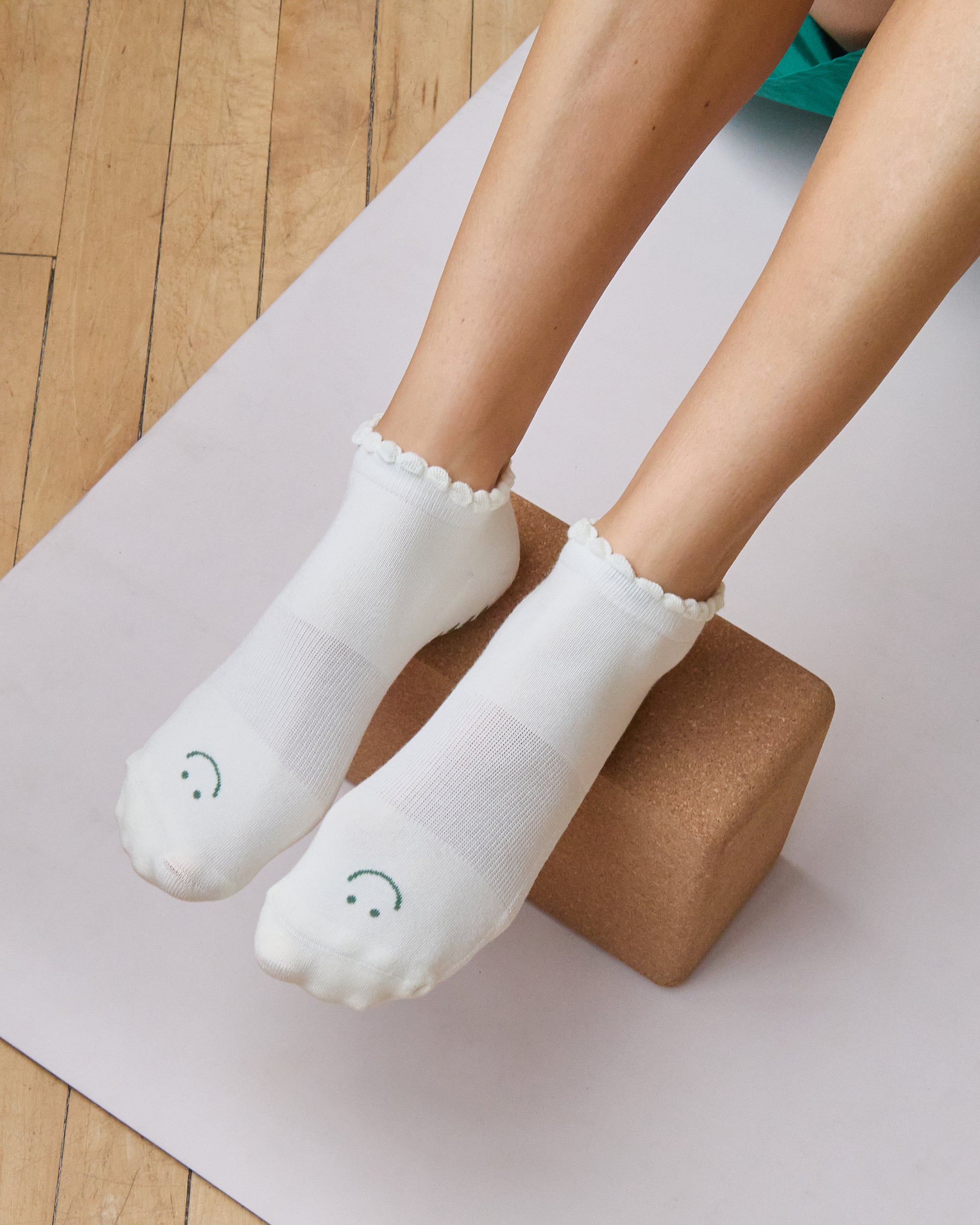 Women wearing white grip socks with green smiley face for Pilates, Barre, Yoga, and beyond.