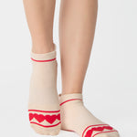 Women wearing a solid off white full foot grip sock with a string of red hearts , made for pilates, barre, yoga, and beyond.