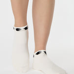 Woman wearing a white sold color full foot grip sock with crows circling the cuff. Made for pilates, barre, yoga, and beyond.