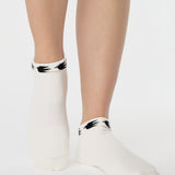 Woman wearing a white sold color full foot grip sock with crows circling the cuff. Made for pilates, barre, yoga, and beyond.