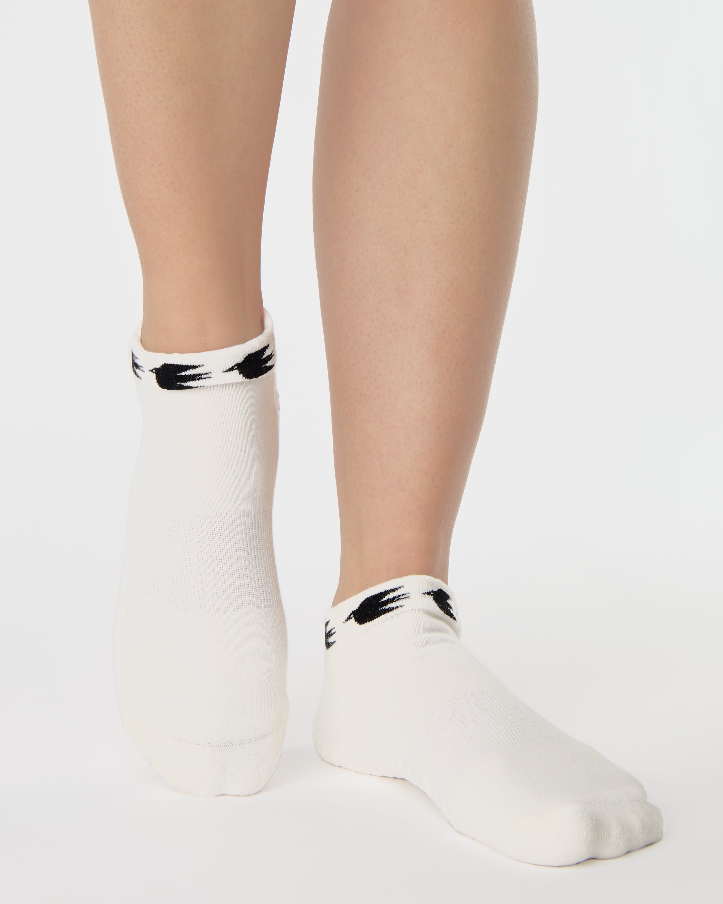 Woman wearing a white sold color full foot grip sock with crows circling the cuff. Made for pilates, barre, yoga, and beyond.