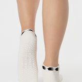 Woman wearing a white sold color full foot grip sock with crows circling the cuff. Made for pilates, barre, yoga, and beyond.