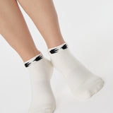 Woman wearing a white sold color full foot grip sock with crows circling the cuff. Made for pilates, barre, yoga, and beyond.