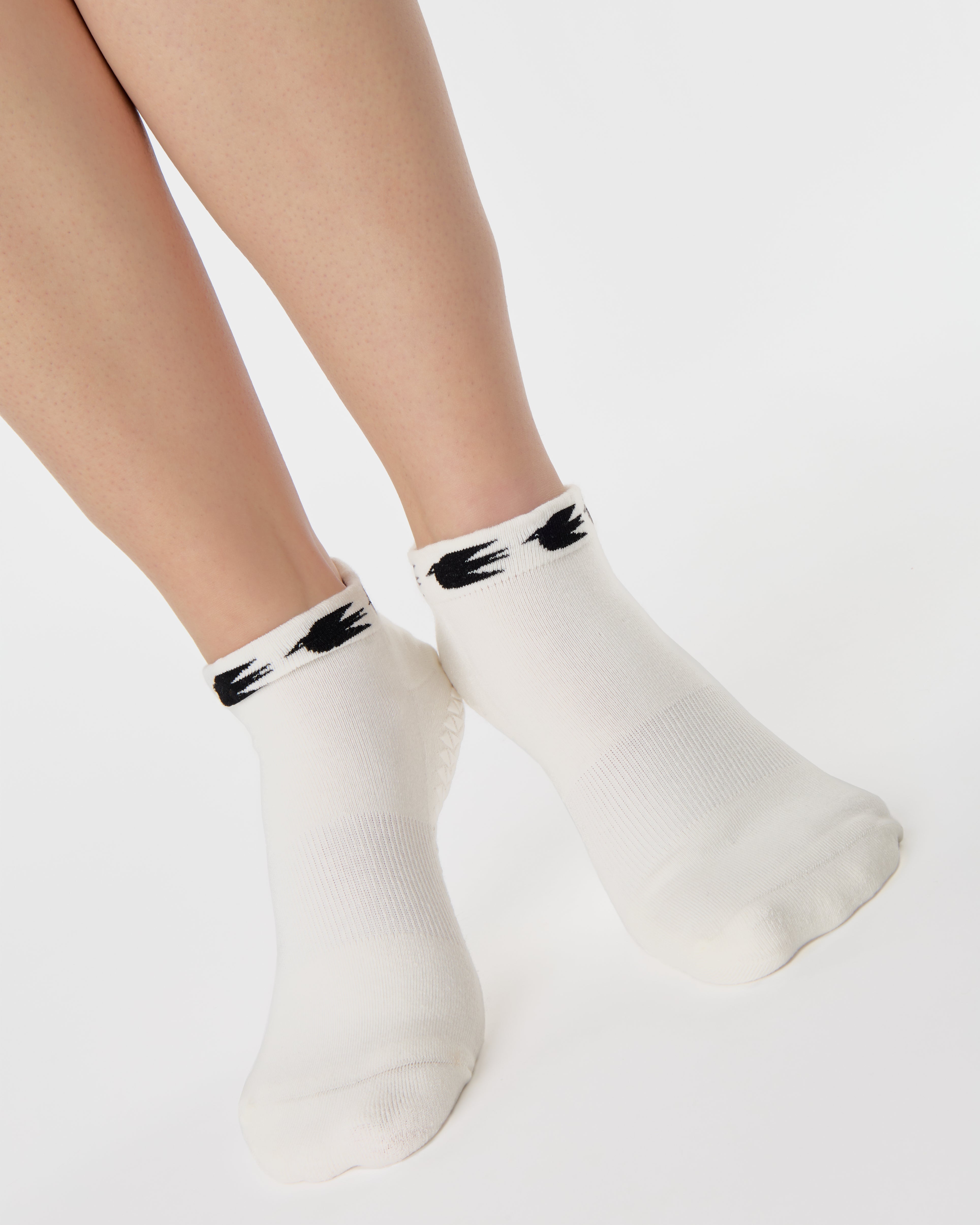 Woman wearing a white sold color full foot grip sock with crows circling the cuff. Made for pilates, barre, yoga, and beyond.