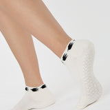 Woman wearing a white sold color full foot grip sock with crows circling the cuff. Made for pilates, barre, yoga, and beyond.