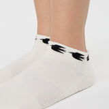 Woman wearing a white sold color full foot grip sock with crows circling the cuff. Made for pilates, barre, yoga, and beyond.