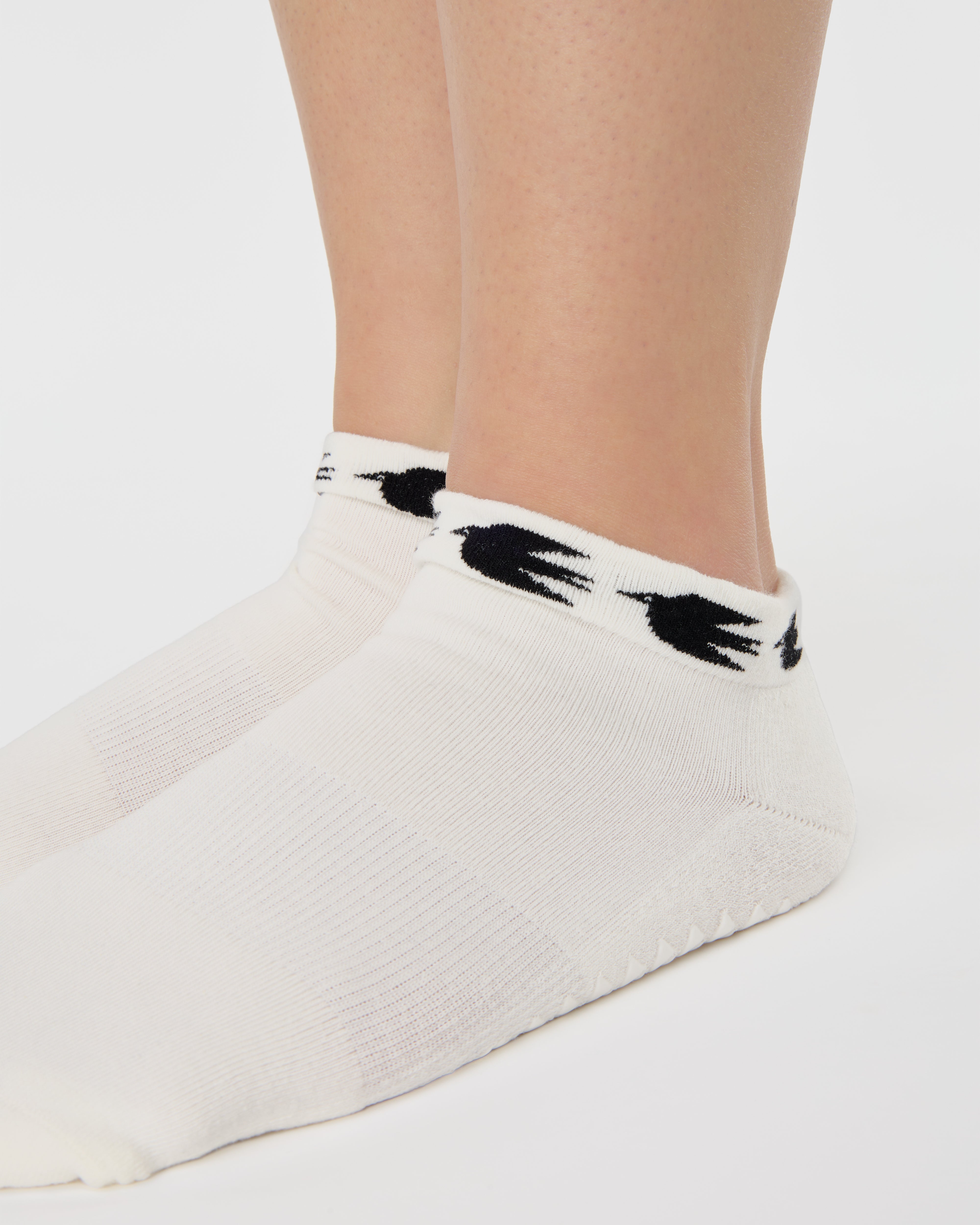 Woman wearing a white sold color full foot grip sock with crows circling the cuff. Made for pilates, barre, yoga, and beyond.