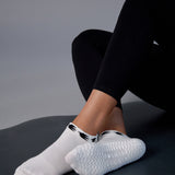 Woman on yoga mat wearing a white sold color full foot grip sock with crows circling the cuff. Made for pilates, barre, yoga, and beyond.