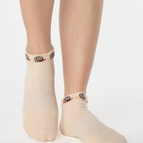 Woman wearing a beige sold color full foot grip sock with snails circling the cuff. Made for pilates, barre, yoga, and beyond.
