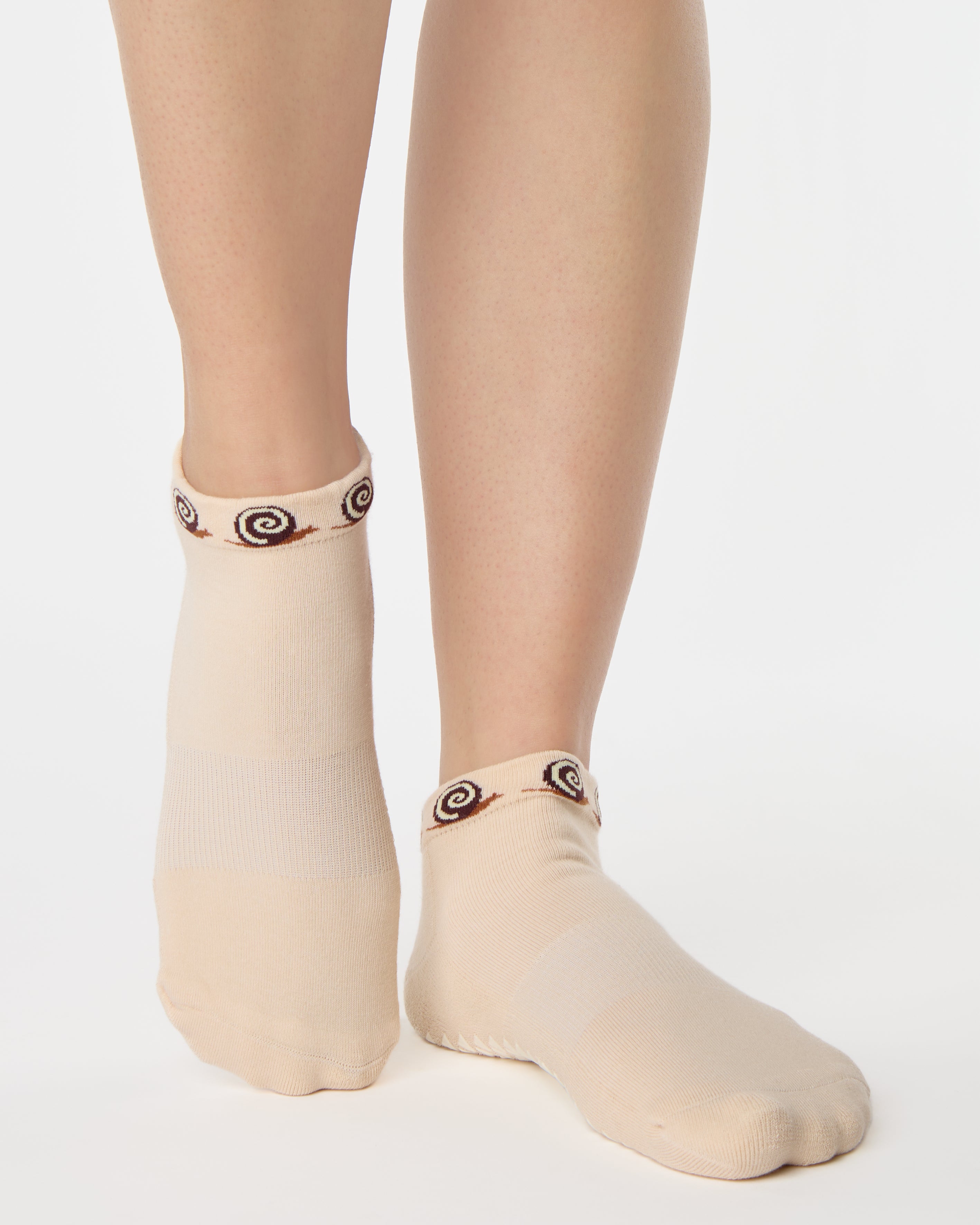 Woman wearing a beige sold color full foot grip sock with snails circling the cuff. Made for pilates, barre, yoga, and beyond.