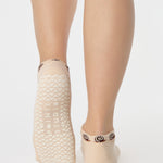 Woman wearing a beige sold color full foot grip sock with snails circling the cuff. Made for pilates, barre, yoga, and beyond.