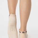 Woman wearing a beige sold color full foot grip sock with snails circling the cuff. Made for pilates, barre, yoga, and beyond.
