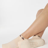 Woman wearing a beige sold color full foot grip sock with snails circling the cuff. Made for pilates, barre, yoga, and beyond.