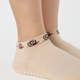 Woman wearing a beige sold color full foot grip sock with snails circling the cuff. Made for pilates, barre, yoga, and beyond.