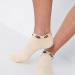 Woman wearing a beige sold color full foot grip sock with snails circling the cuff. Made for pilates, barre, yoga, and beyond.