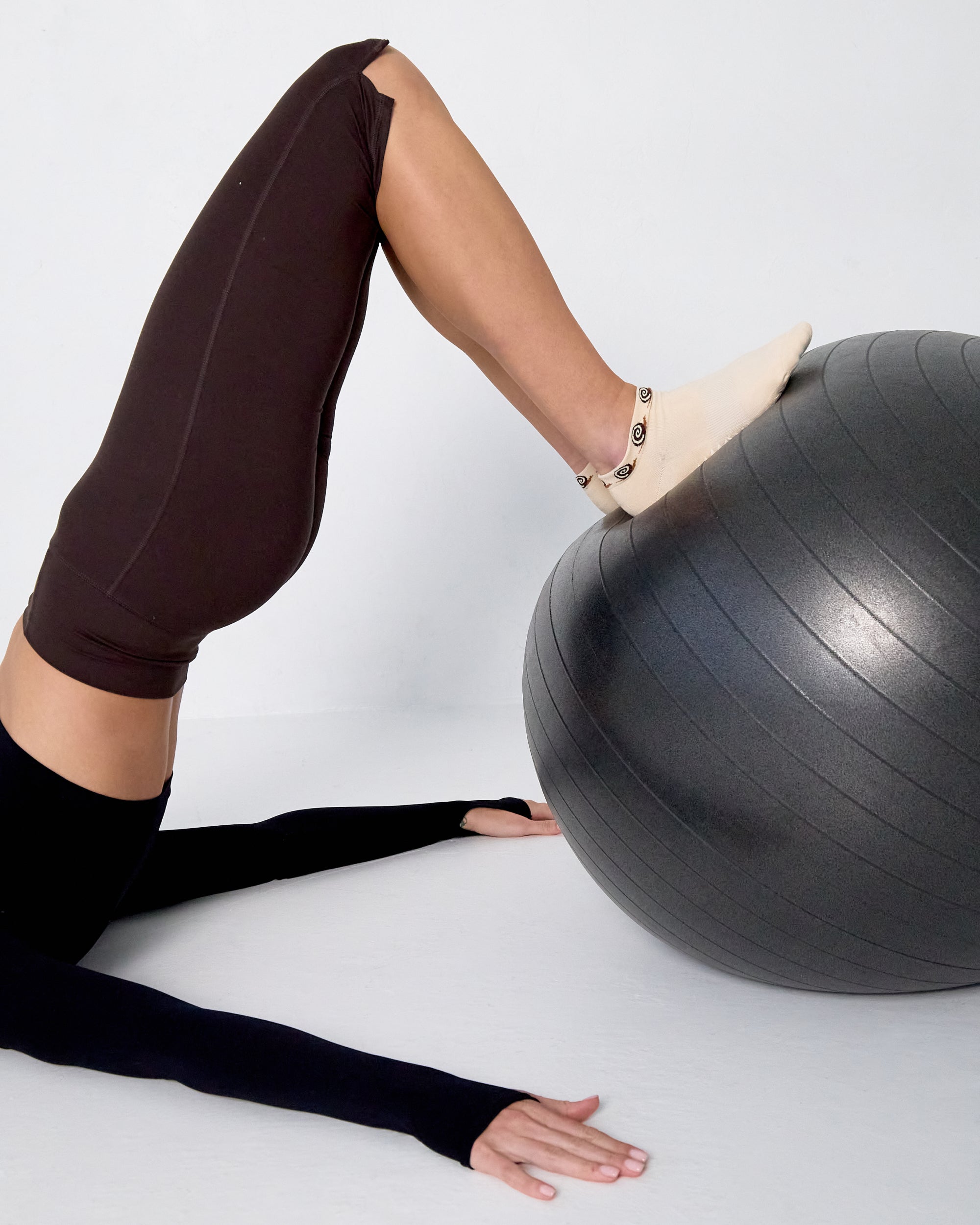 Woman wearing a beige sold color full foot grip sock with snails circling the cuff. Made for pilates, barre, yoga, and beyond.