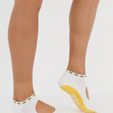 Woman wearing solid white strap grip sock with bumble bees wrapping around the scalloped cuff, made for pilates, barre, yoga, and beyond. 