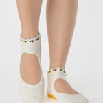 Woman wearing solid white strap grip sock with bumble bees wrapping around the scalloped cuff, made for pilates, barre, yoga, and beyond. 