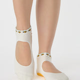 Woman wearing solid white strap grip sock with bumble bees wrapping around the scalloped cuff, made for pilates, barre, yoga, and beyond. 