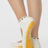 Woman wearing solid white strap grip sock with bumble bees wrapping around the scalloped cuff, made for pilates, barre, yoga, and beyond. 