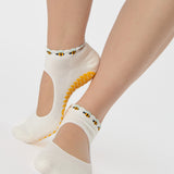 Woman wearing solid white strap grip sock with bumble bees wrapping around the scalloped cuff, made for pilates, barre, yoga, and beyond. 