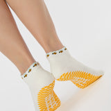 Woman wearing solid white strap grip sock with bumble bees wrapping around the scalloped cuff, made for pilates, barre, yoga, and beyond. 