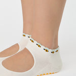 Woman wearing solid white strap grip sock with bumble bees wrapping around the scalloped cuff, made for pilates, barre, yoga, and beyond. 