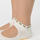 Woman wearing solid white strap grip sock with bumble bees wrapping around the scalloped cuff, made for pilates, barre, yoga, and beyond. 