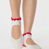 Woman wearing solid white strap grip sock with red heart wrapping around the scalloped cuff, made for pilates, barre, yoga, and beyond. 