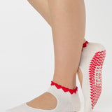 Woman wearing solid white strap grip sock with red heart wrapping around the scalloped cuff, made for pilates, barre, yoga, and beyond. 