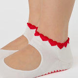 Woman wearing solid white strap grip sock with red heart wrapping around the scalloped cuff, made for pilates, barre, yoga, and beyond. 