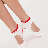 Woman wearing solid white strap grip sock with red heart wrapping around the scalloped cuff, made for pilates, barre, yoga, and beyond. 