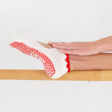 Woman on a barre wearing solid white strap grip sock with red heart wrapping around the scalloped cuff, made for pilates, barre, yoga, and beyond. 