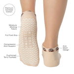 Woman wearing a beige sold color full foot grip sock with snails circling the cuff. Made for pilates, barre, yoga, and beyond. With product features listed.