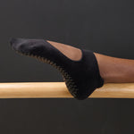 Woman wearing a solid black strap grip sock, made for pilates, barre, yoga, and beyond. 