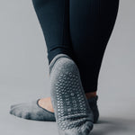 Woman wearing a solid charcoal grey strap grip sock, made for pilates, barre, yoga, and beyond. 