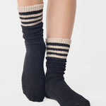 Women wearing a black mid-weight knit grip sock that scrunches with beige stripes on the ankle part, made for Pilates, Barre, Yoga, and Beyond. 