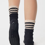Women wearing a black mid-weight knit grip sock that scrunches with beige stripes on the ankle part, made for Pilates, Barre, Yoga, and Beyond. 