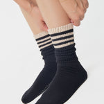 Women wearing a black mid-weight knit grip sock that scrunches with beige stripes on the ankle part, made for Pilates, Barre, Yoga, and Beyond. 