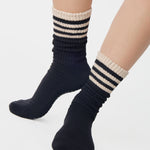 Women wearing a black mid-weight knit grip sock that scrunches with beige stripes on the ankle part, made for Pilates, Barre, Yoga, and Beyond. 