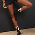 Women wearing a black mid-weight knit grip sock that scrunches with beige stripes on the ankle part, made for Pilates, Barre, Yoga, and Beyond. 